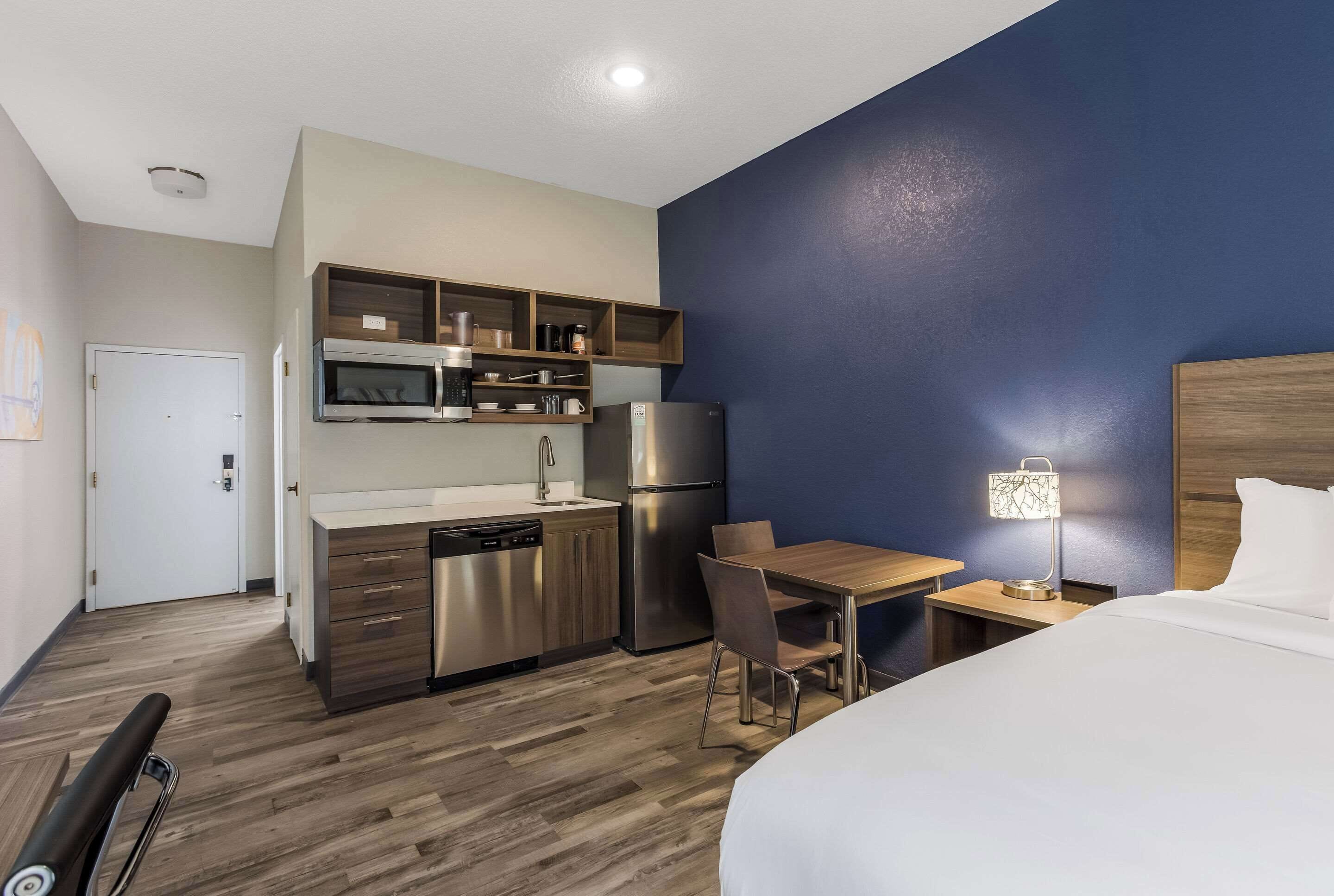 Une chambre d’hôtel de taille réduite, équipée d’une kitchenette, d’un lit, d’un bureau et d’une chaise.
