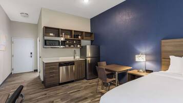 Une chambre d’hôtel de taille réduite, équipée d’une kitchenette, d’un lit, d’un bureau et d’une chaise.