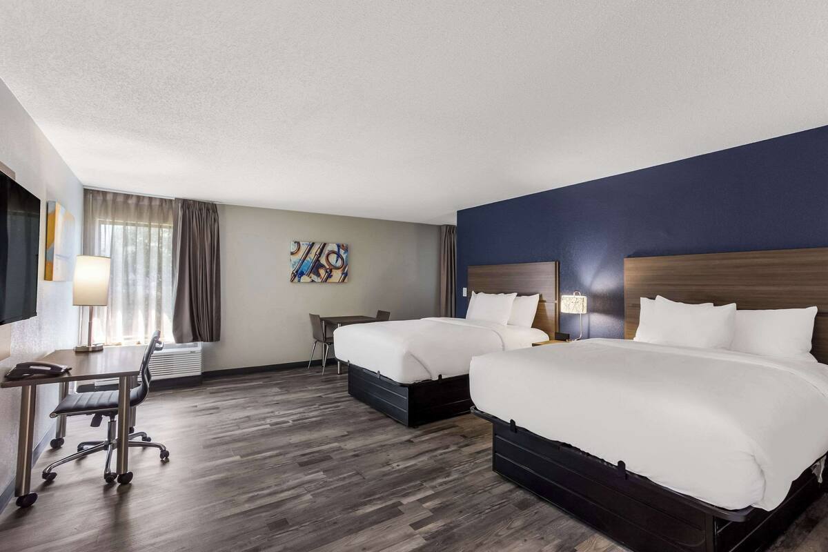 Une chambre d’hôtel avec deux lits, un bureau, une chaise et un tableau au mur.