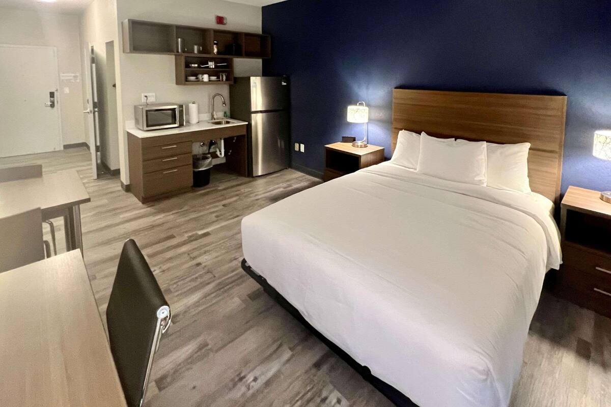 Une chambre d’hôtel équipée d’un lit, d’un bureau, d’un four à micro-ondes, d’un réfrigérateur, d’une table de chevet et d’une lampe.