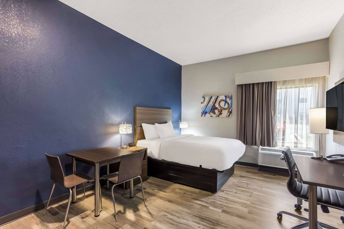 Une chambre d’hôtel avec un lit, un bureau, une chaise et une grande fenêtre avec des rideaux.