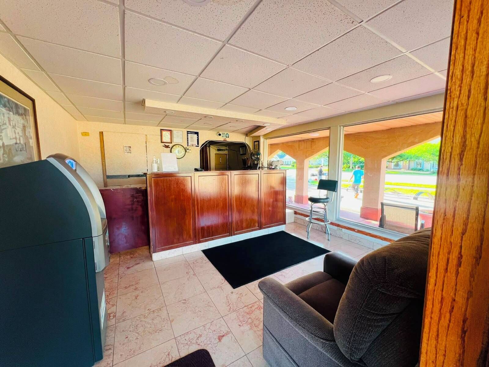 A reception area with a wooden desk, a black reception counter, a black rug, and a seating area with a brown chair.