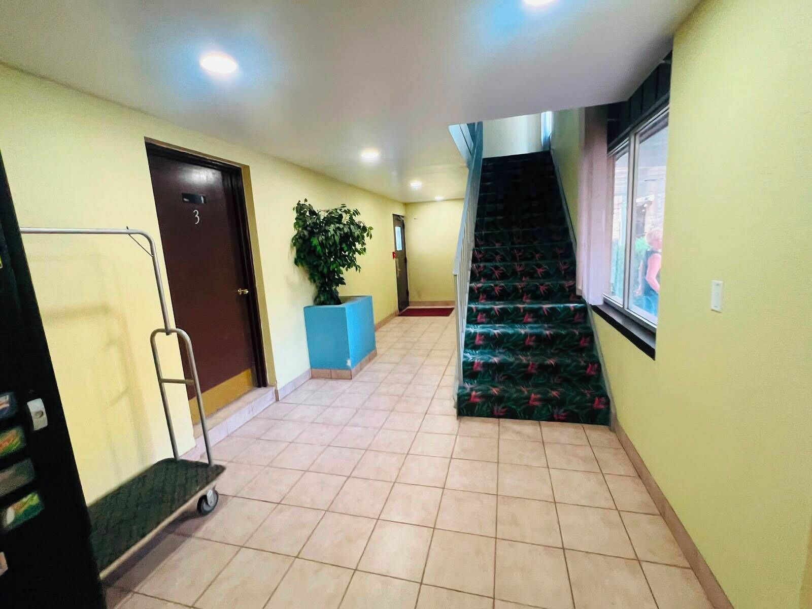 A hallway with a tiled floor, a blue planter, a door, a staircase, and a window.