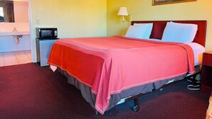 A hotel room with a bed, a nightstand, a lamp, a framed picture on the wall, and a microwave.