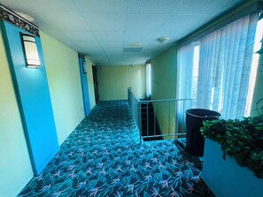 A hallway with patterned carpet, a trash bin, and a potted plant.