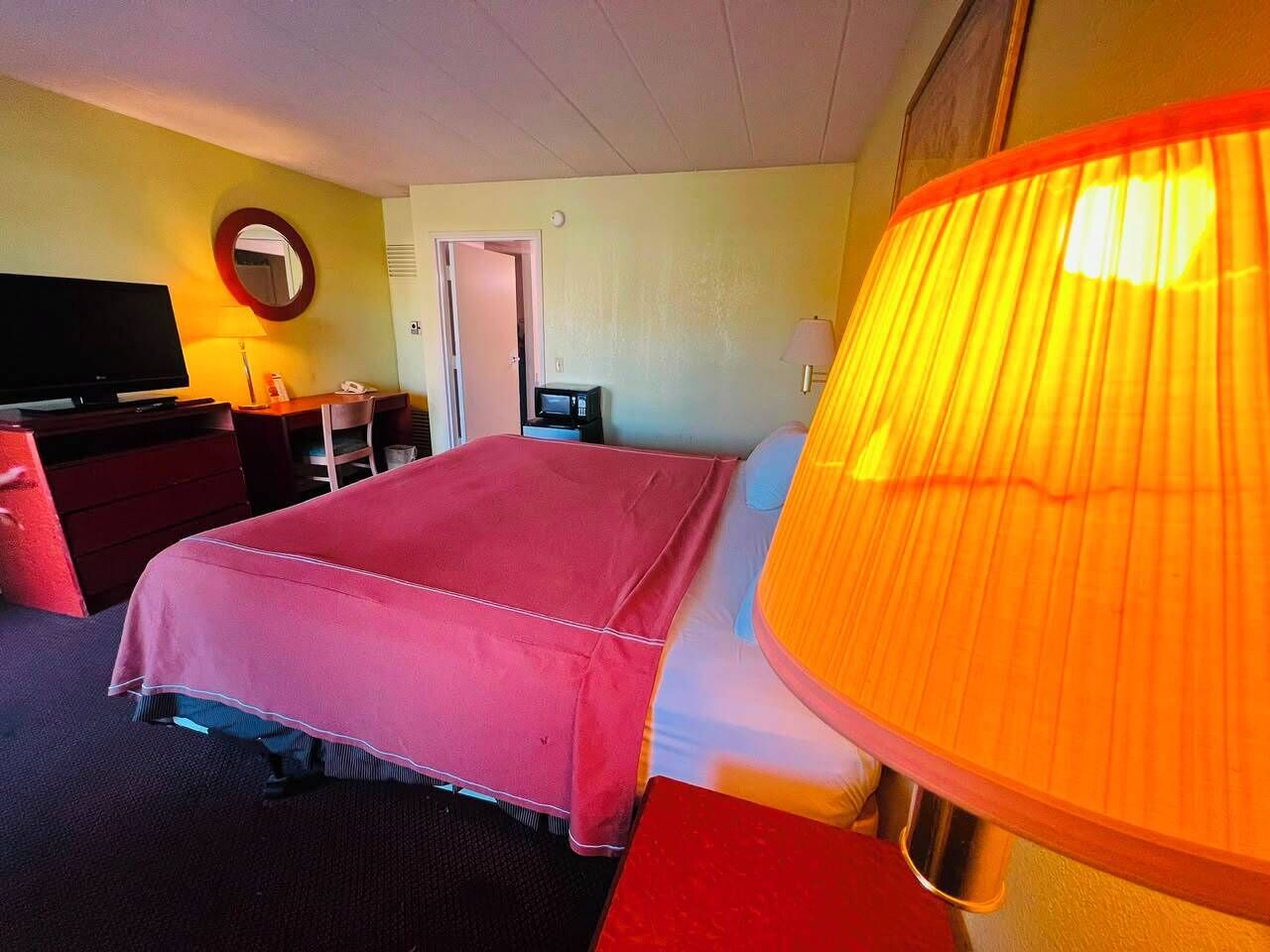 A hotel room with a bed, a television, a desk, and a lamp.