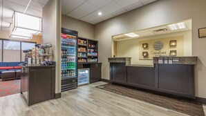 A hotel reception area with a Coca-Cola refrigerator, snack shelves, and a seating area with a red carpet. - Comfort Inn Alton near I-255 (Alton)
