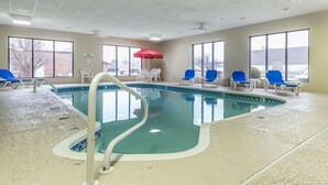 An indoor swimming pool with clear blue water, surrounded by white and blue lounge chairs, and a red umbrella providing shade. - Comfort Inn Alton near I-255 (Alton)