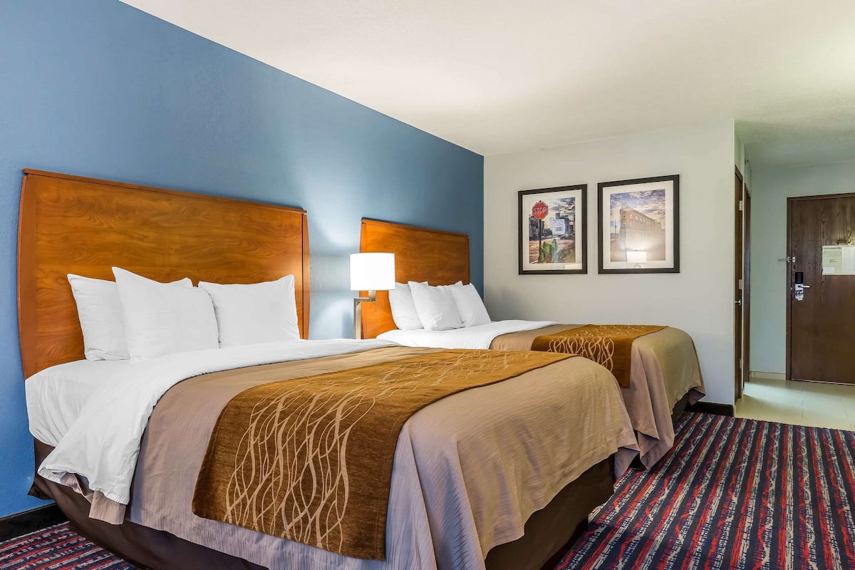 A hotel room with two beds, a patterned carpet, and a door to the right.