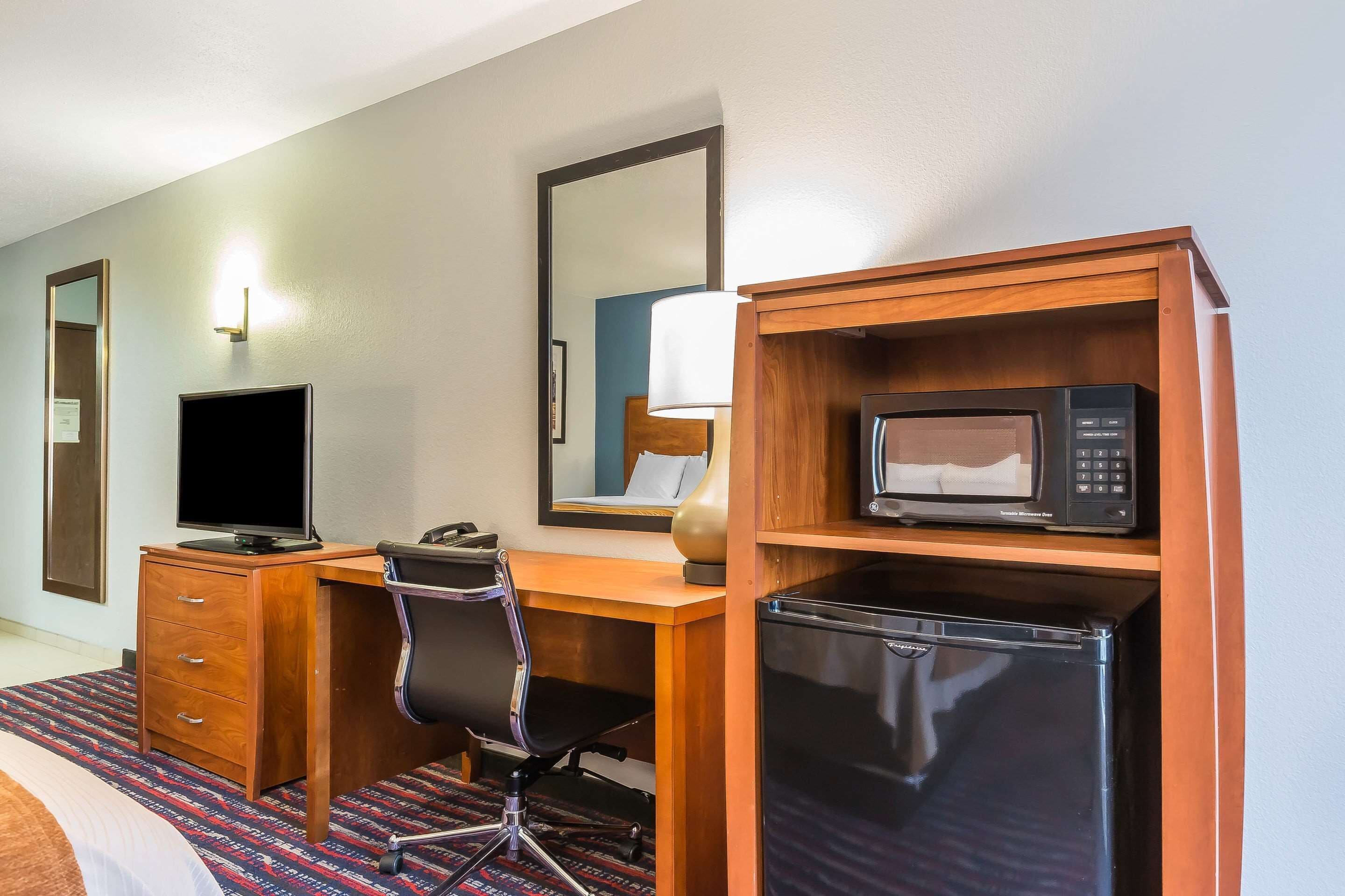 Une chambre d’hôtel équipée d’un bureau en bois, d’une télévision, d’un four à micro-ondes, d’un réfrigérateur, d’une chaise et d’un lit.