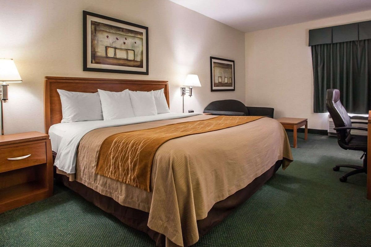 A hotel room with a large bed, two bedside tables, a desk, a chair, and two framed pictures on the wall.