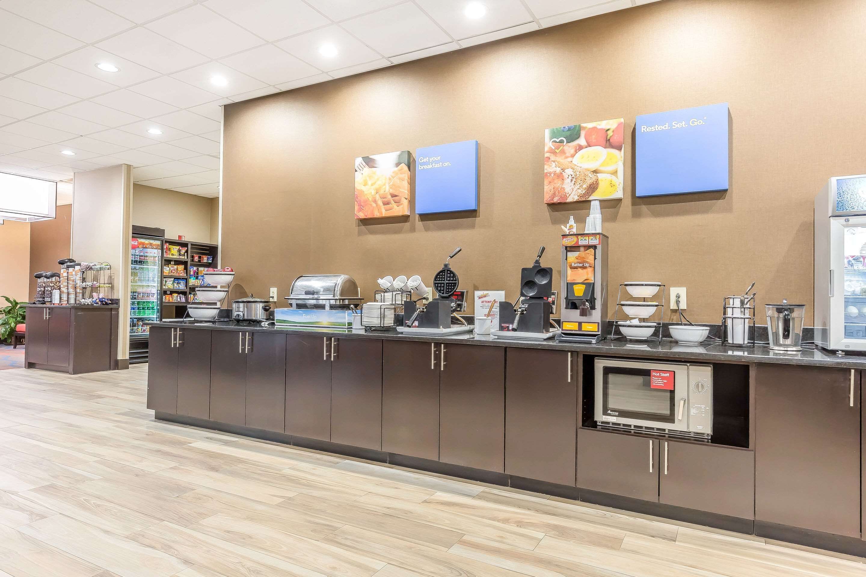 A breakfast bar with a microwave, coffee machines, and a variety of food items.