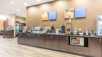 A breakfast bar with a microwave, coffee machines, and a variety of food items.
