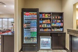 Máquina expendedora con Coca-Cola, Doritos y otros snacks, un refrigerador con bebidas y un pequeño congelador con pasteles.