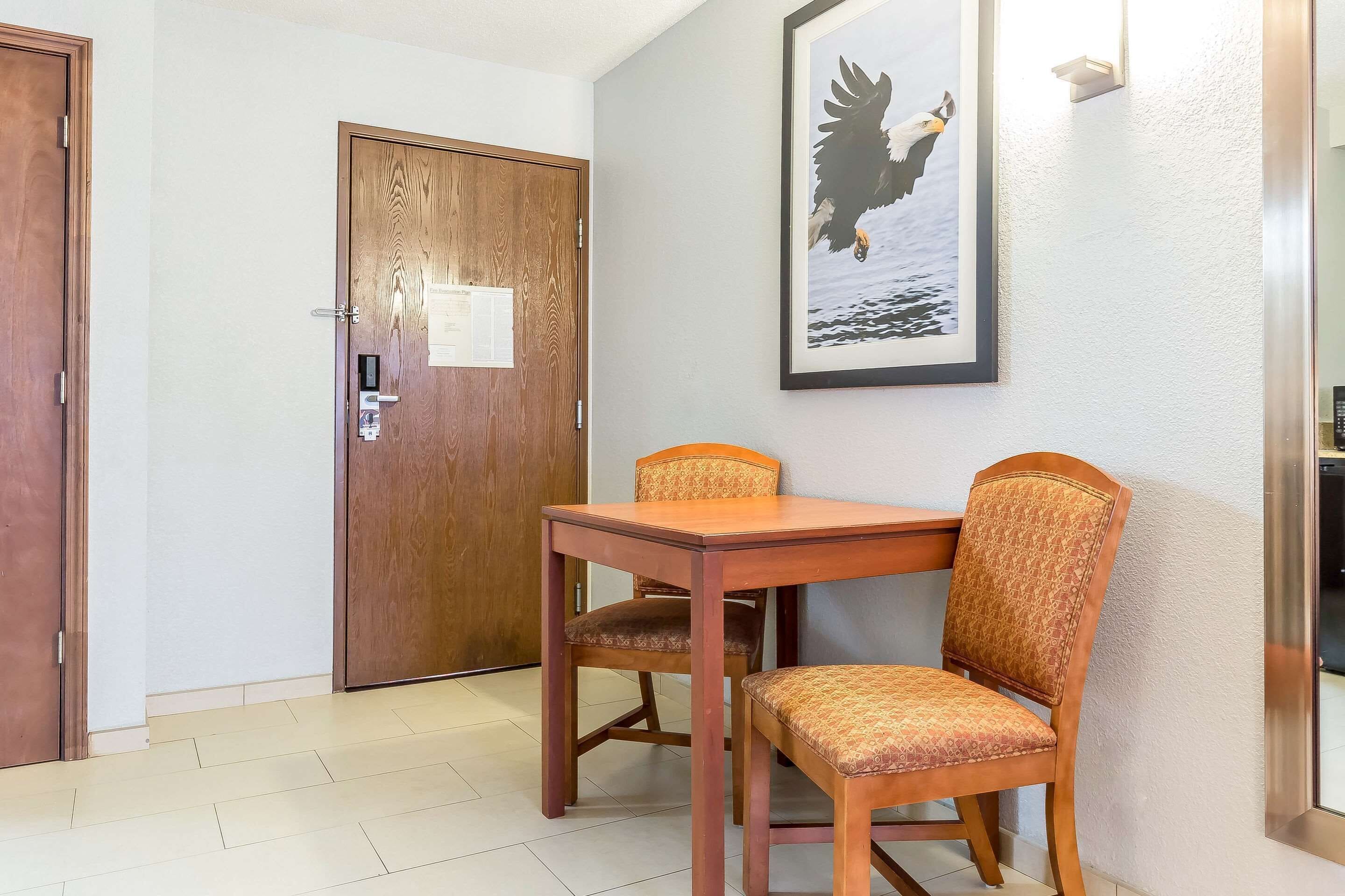 A hotel room with a wooden door, a framed picture of an eagle, and a dining table with two chairs.