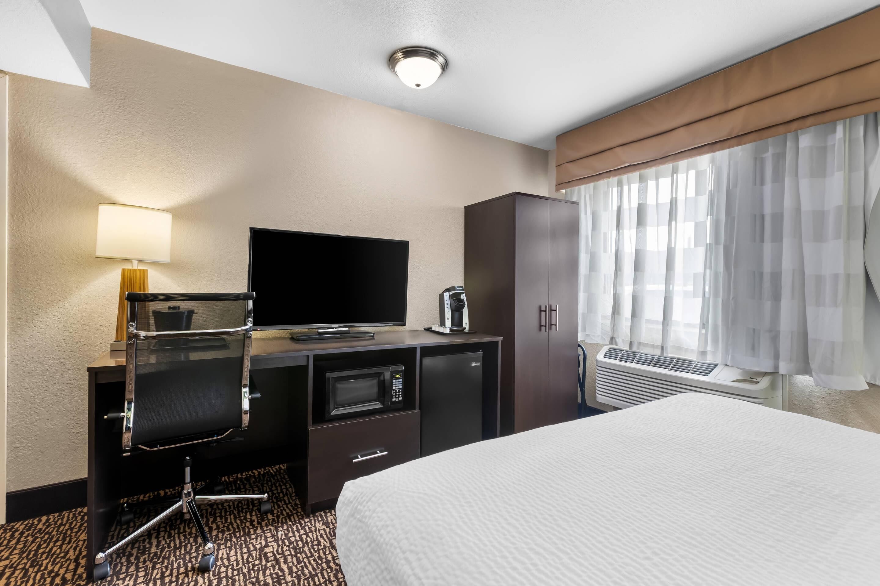 Une chambre d’hôtel équipée d’un lit, d’un bureau avec une télévision, d’une machine à café, d’un four à micro-ondes et d’un radiateur.