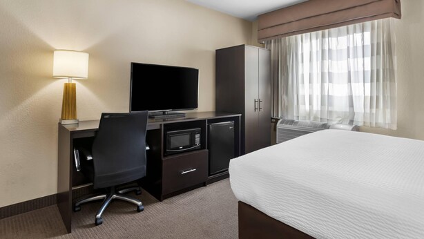 A hotel room with a bed, a desk with a television, a microwave, a refrigerator, a chair, and a window with curtains. - Sleep Inn Nampa near Idaho Center (Nampa)