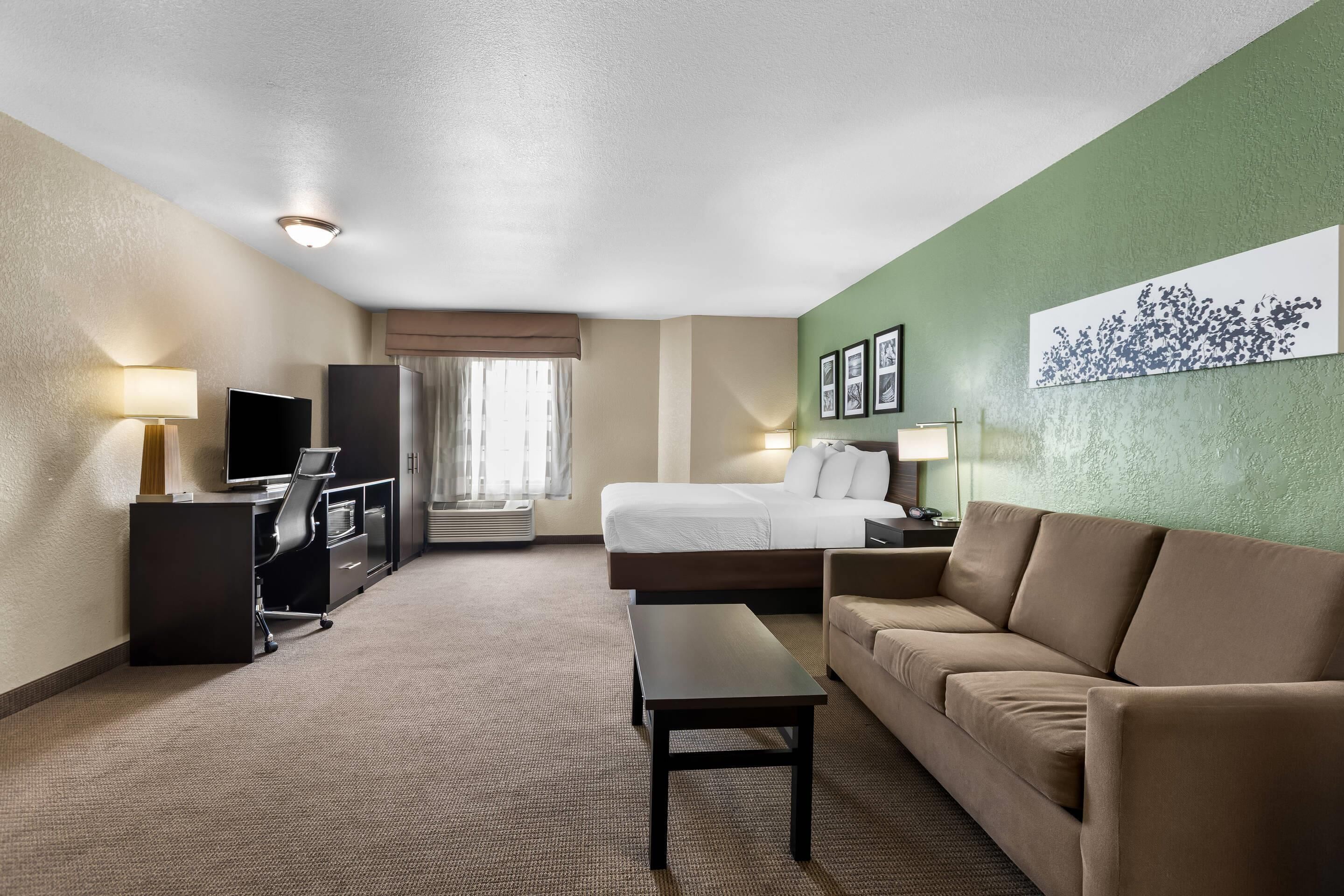 A hotel room with a bed, a sofa, a desk with a computer, a TV, and a window with curtains.