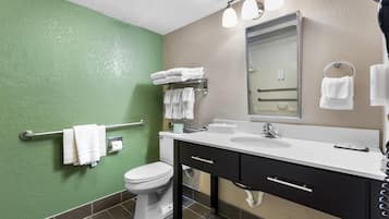 Un baño con pared verde, inodoro blanco y tocador con espejo y lavamanos.