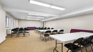Ein Konferenzraum mit mehreren Tischen und Stühlen, weißen Wänden und Deckenleuchten.