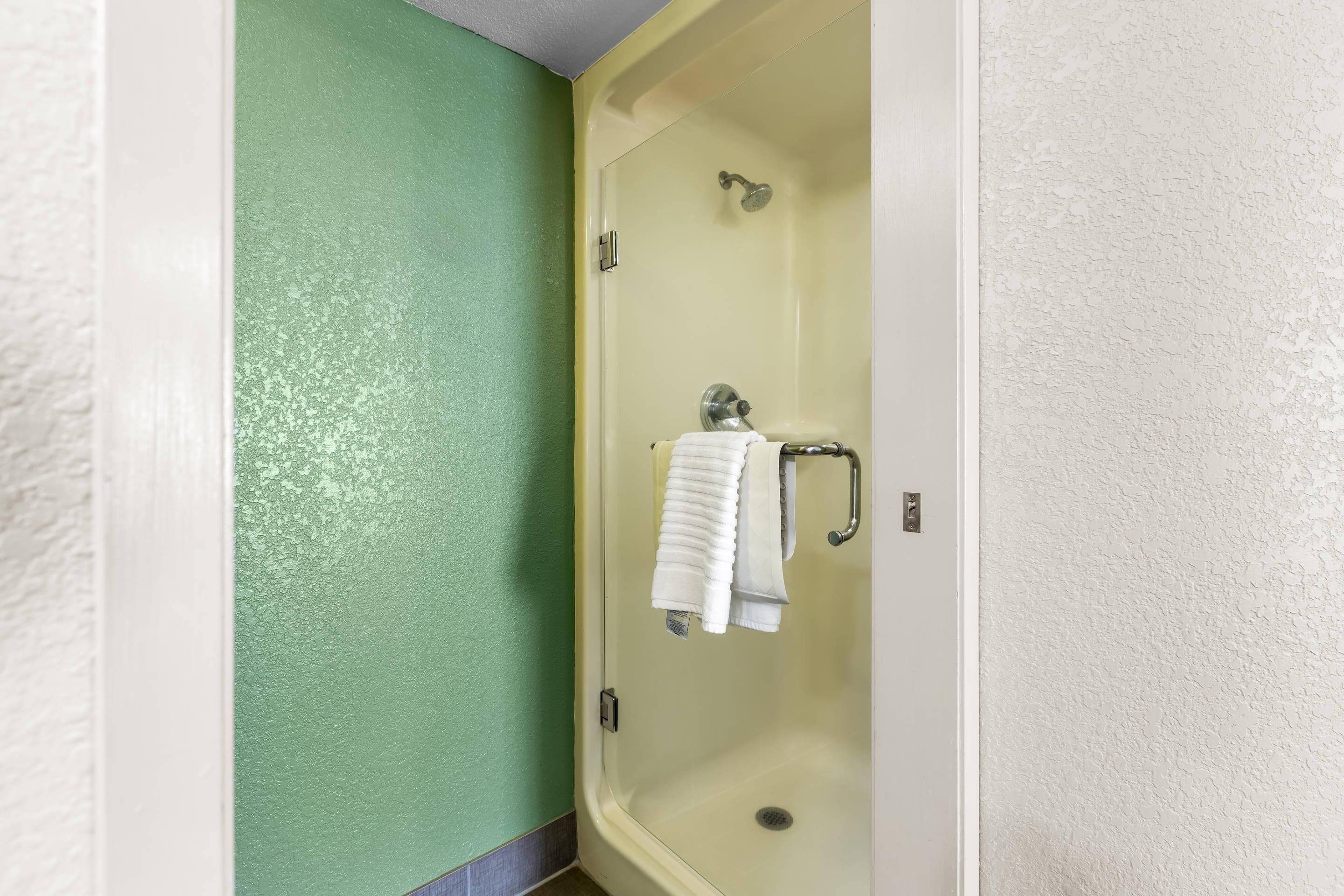 A shower stall with a glass door, a towel rack with a folded towel, and a showerhead.