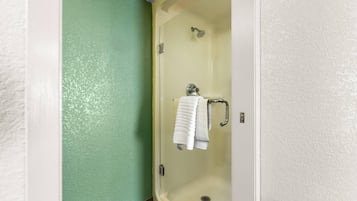 A shower stall with a glass door, a towel rack with a folded towel, and a showerhead.