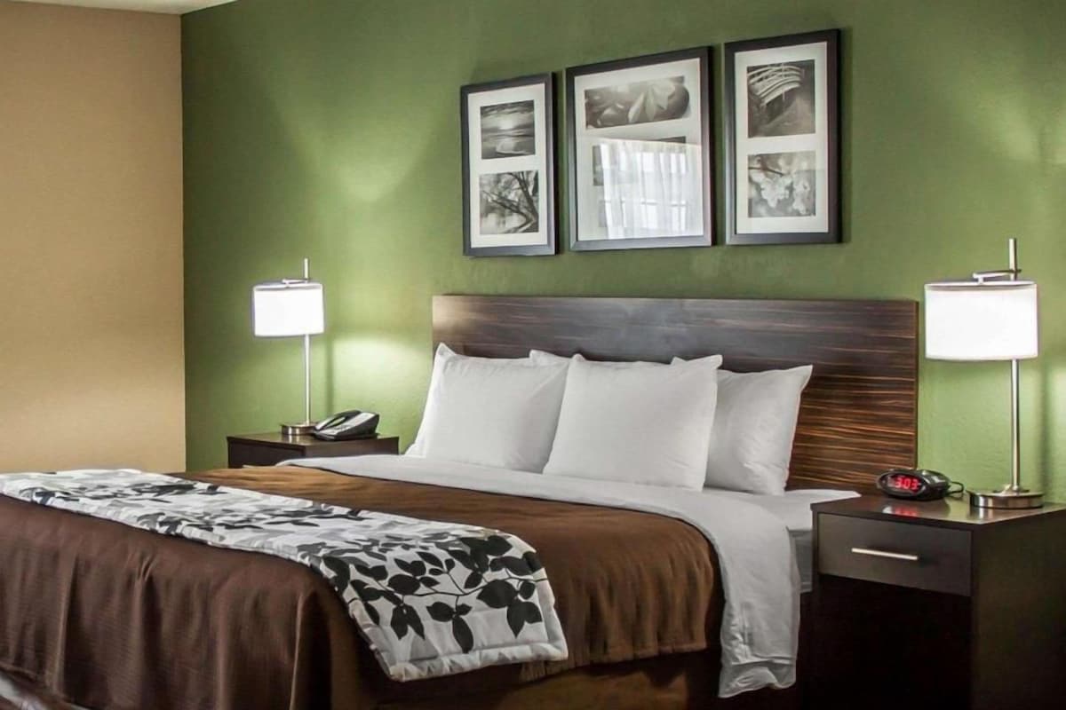 A hotel room with a bed, two bedside tables, a nightstand, a lamp, and framed pictures on the wall.