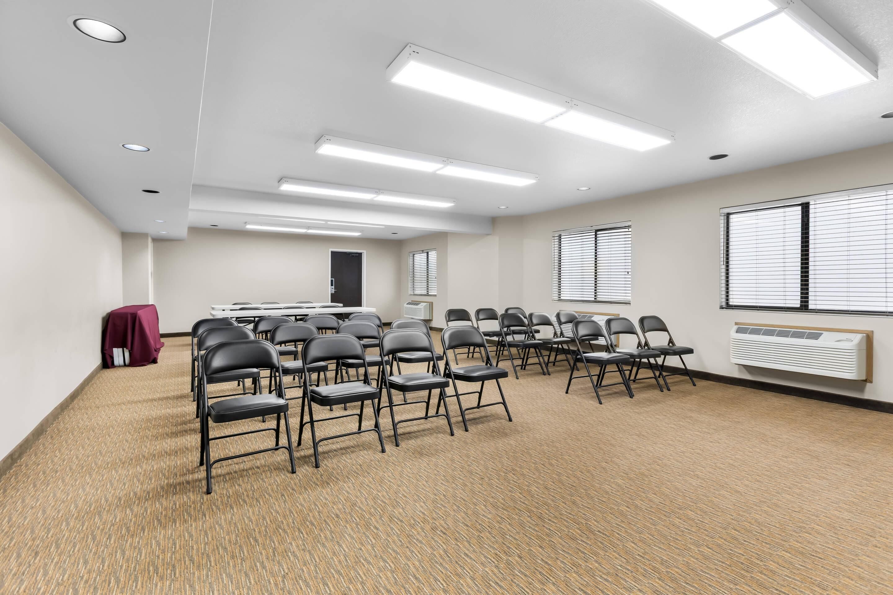 A conference room with a carpeted floor, white walls, and ceiling-mounted fluorescent lights.