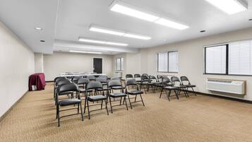 A conference room with a carpeted floor, white walls, and ceiling-mounted fluorescent lights.