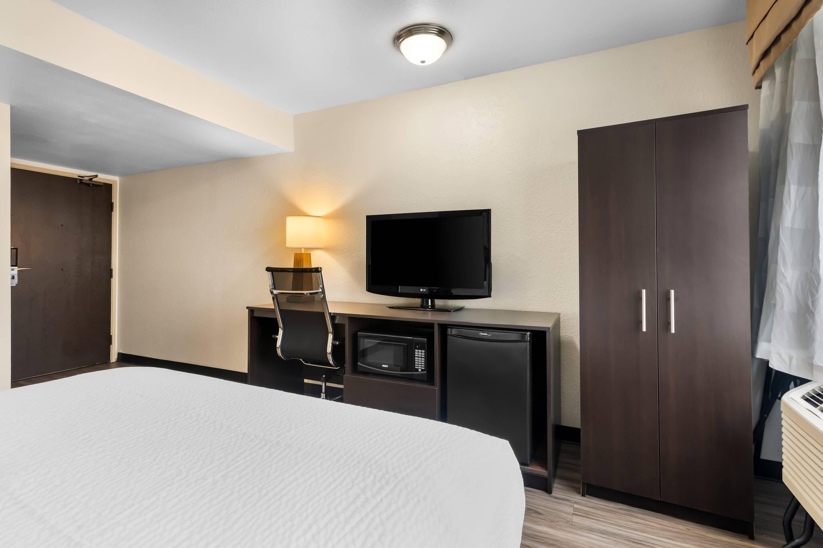 A hotel room with a bed, a television, a minibar, and a wardrobe.