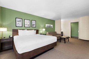 A hotel room with a large bed, a desk, a chair, and a green wall with framed pictures.