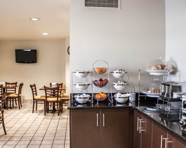 Habitación de hotel con kitchenette, un comedor con sillas de madera y un televisor de pantalla plana montado en la pared.