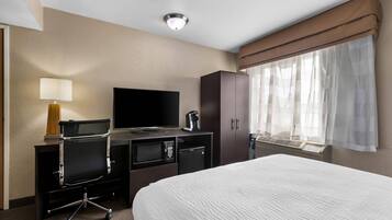Habitación de hotel con cama, escritorio con televisión de pantalla plana, cafetera, microondas y armario.