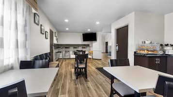 Una habitación de hotel moderna con comedor, cocina y televisor instalado en la pared.