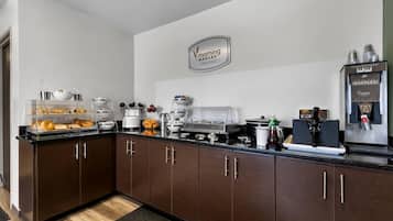 A modern kitchen with a breakfast station, including a coffee machine, waffle maker, and various food items.