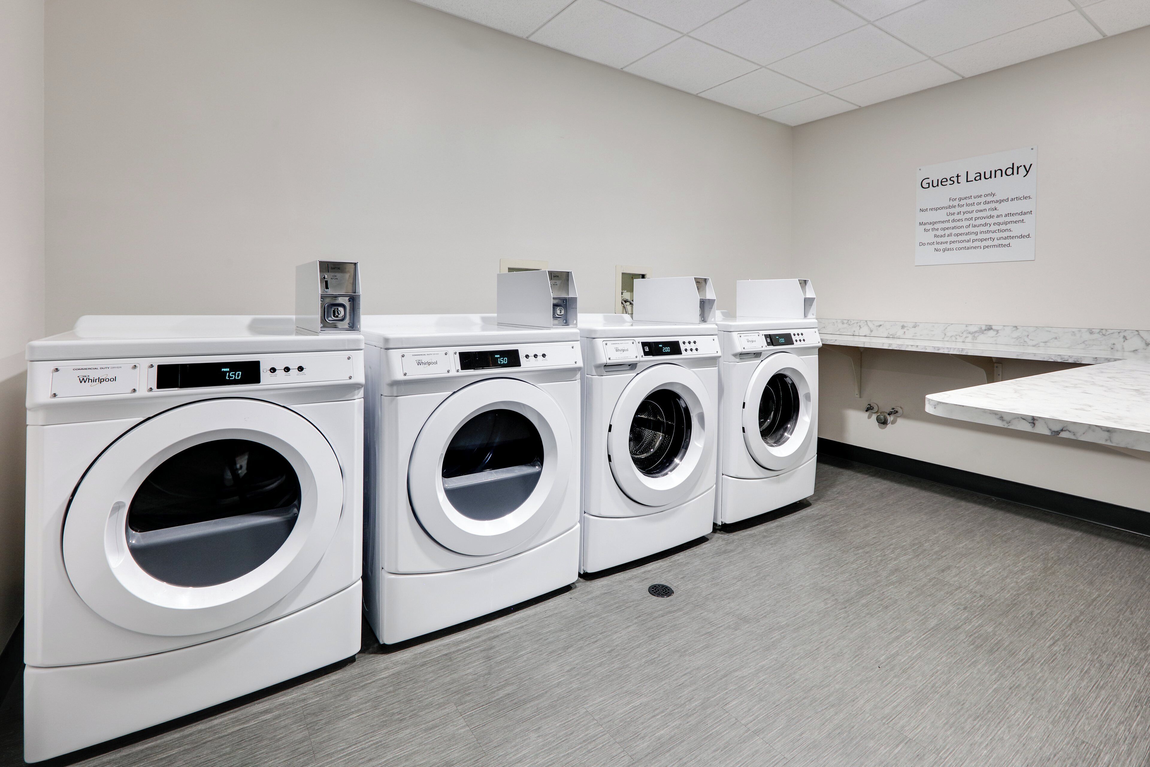 A laundry facility with four Whirlpool washers and dryers, a marble countertop, and a sign indicating guest use.