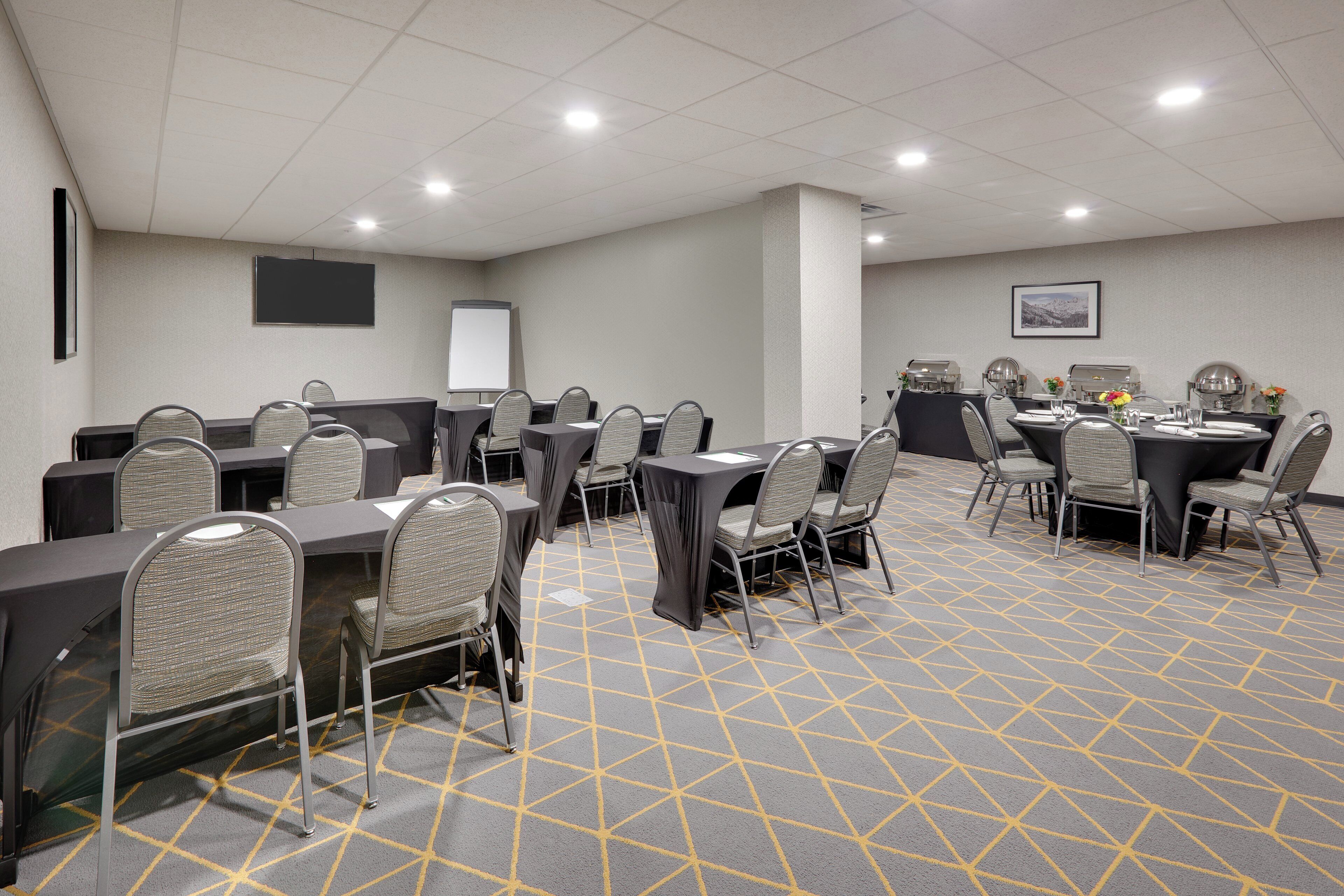 Une salle de conférence équipée de tables et de chaises, d’un téléviseur à écran plat et d’un écran de projection.