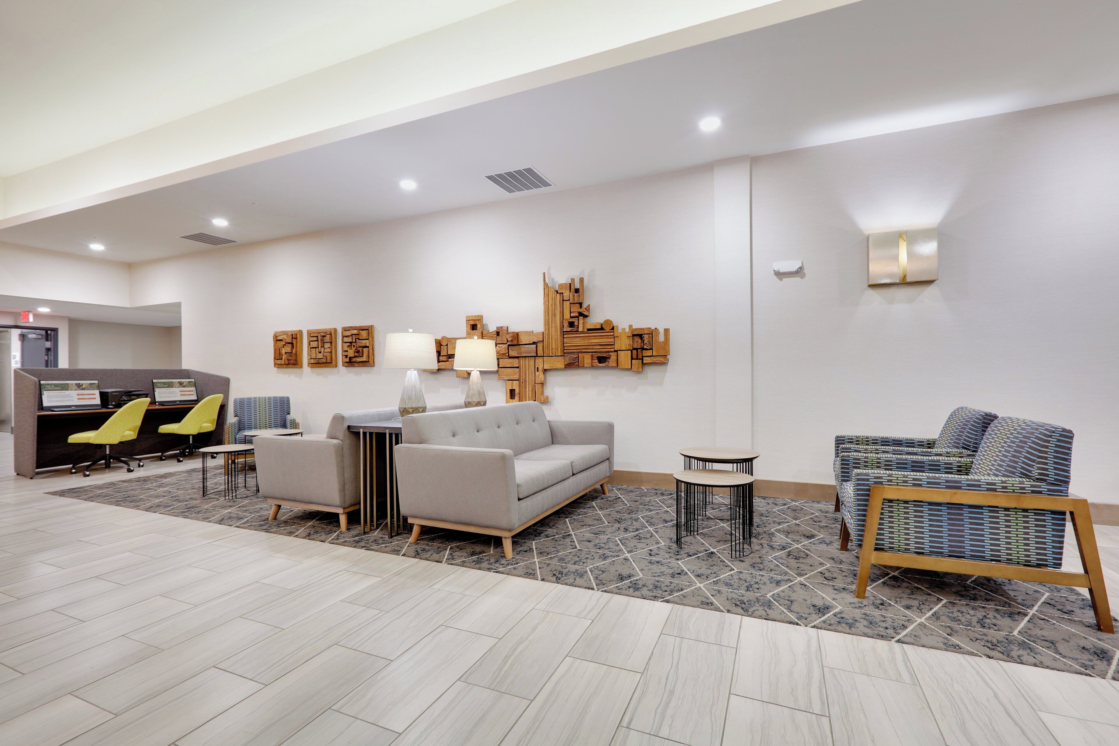 A modern lobby with a grey sofa, two armchairs, a coffee table, and a reception desk with chairs.
