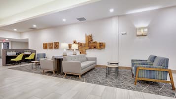 A modern lobby with a grey sofa, two armchairs, a coffee table, and a reception desk with chairs.