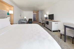 Une chambre d’hôtel avec un grand lit, un bureau avec une chaise, une télévision et un petit coin salon comprenant un canapé et un fauteuil.