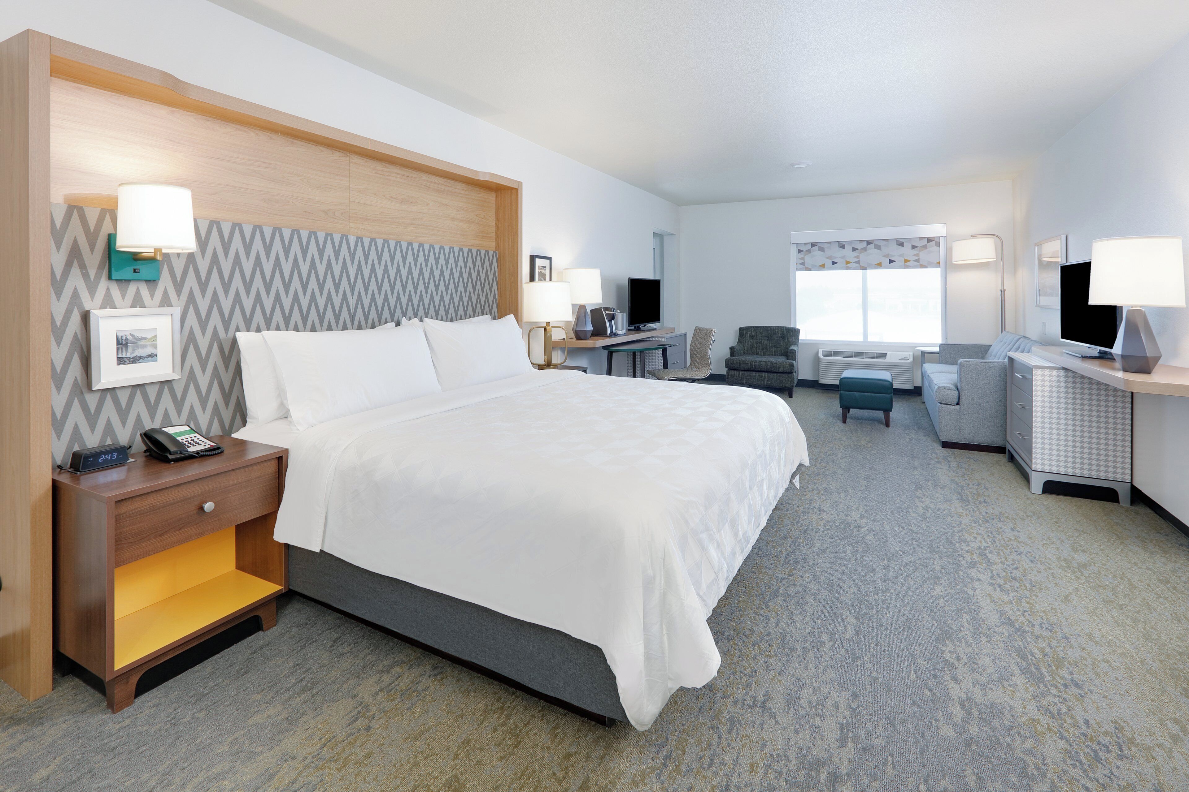 A hotel room with a bed, bedside tables, a desk with a chair, a television, and a window.