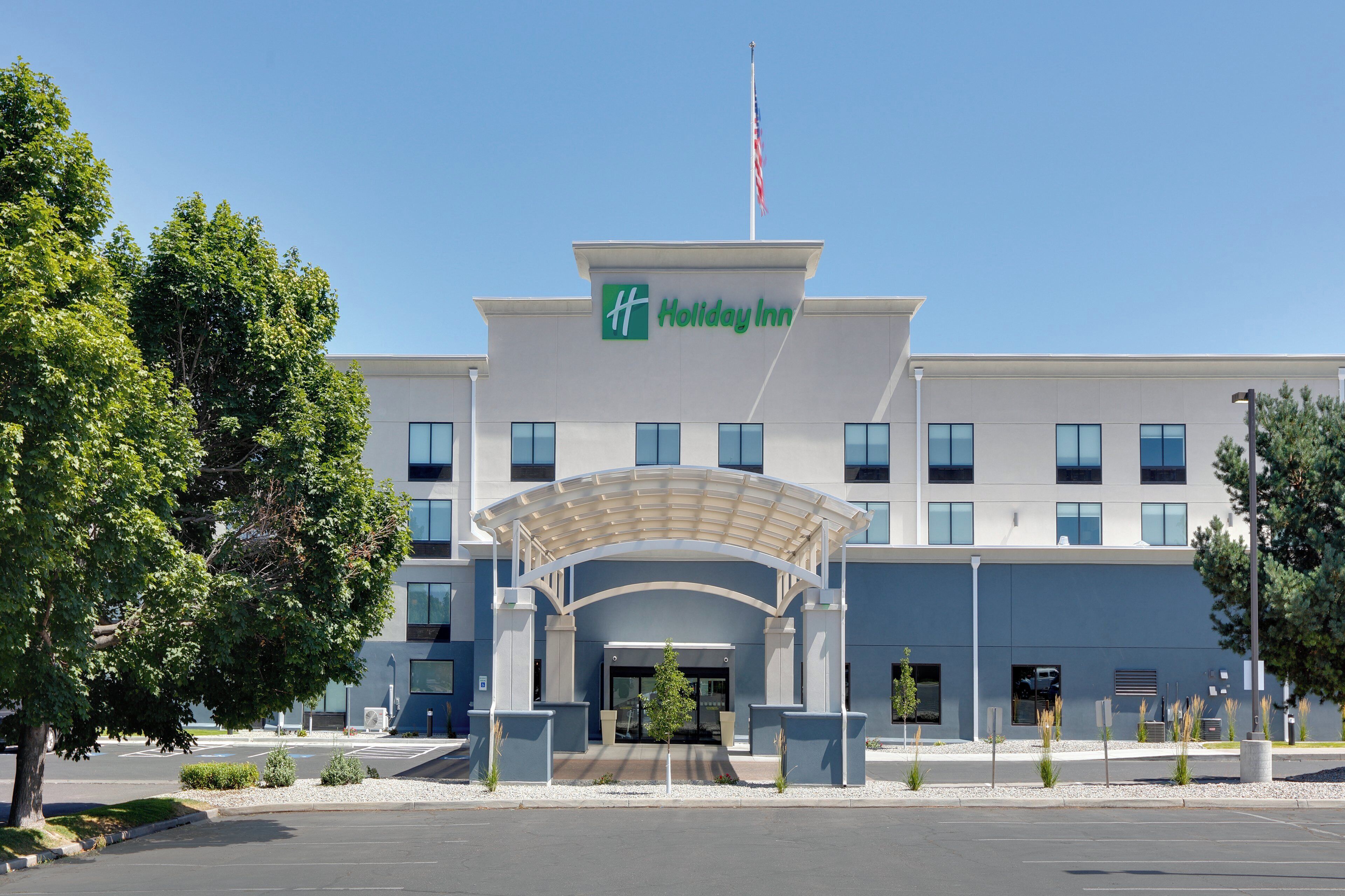 Ett Holiday Inn-hotell med en modern fasad, en inglasad entré och en flaggstång.