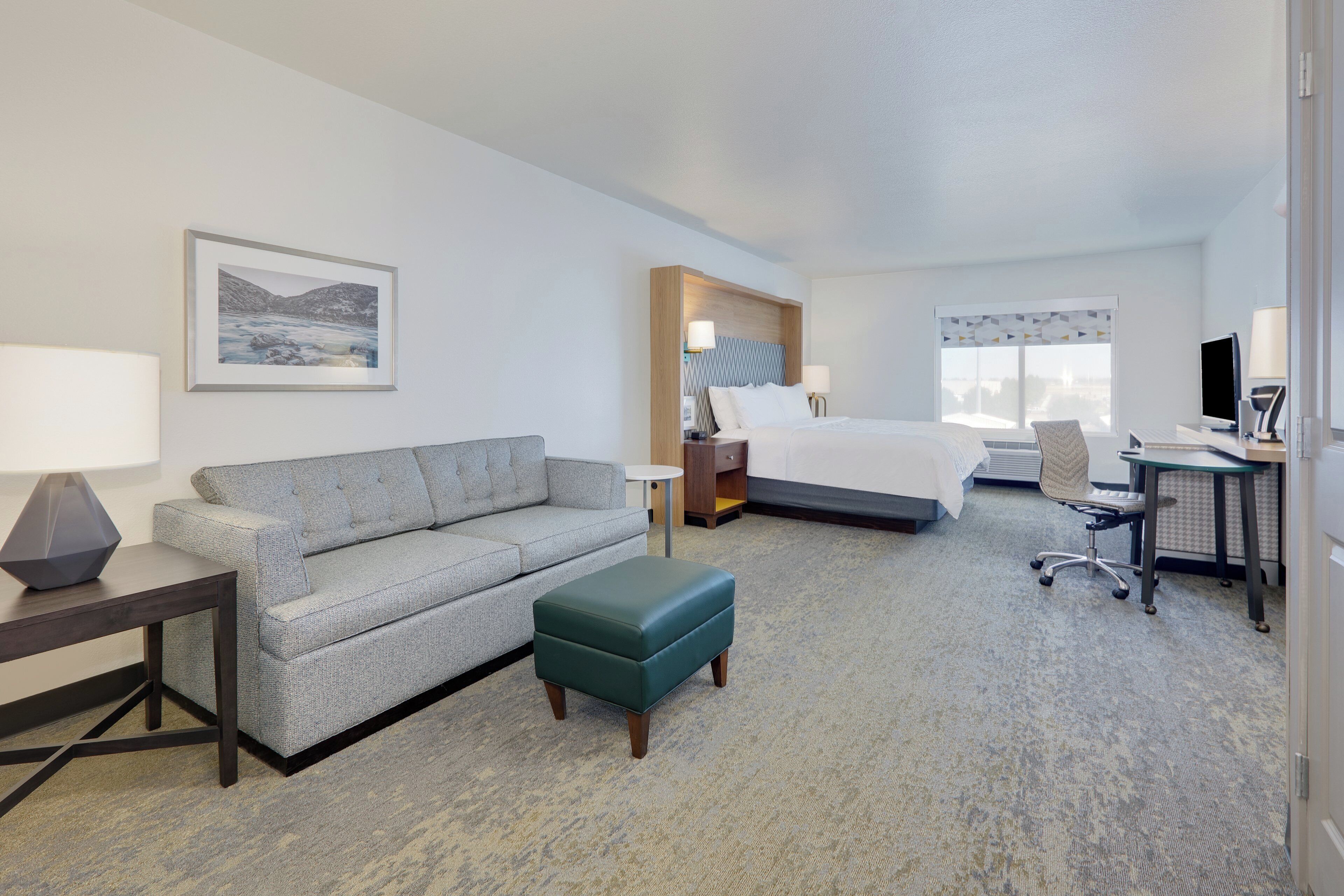 A hotel room with a bed, a desk with a computer, a sofa, a small table, and a chair.