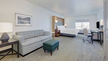 A hotel room with a bed, a desk with a computer, a sofa, a small table, and a chair.