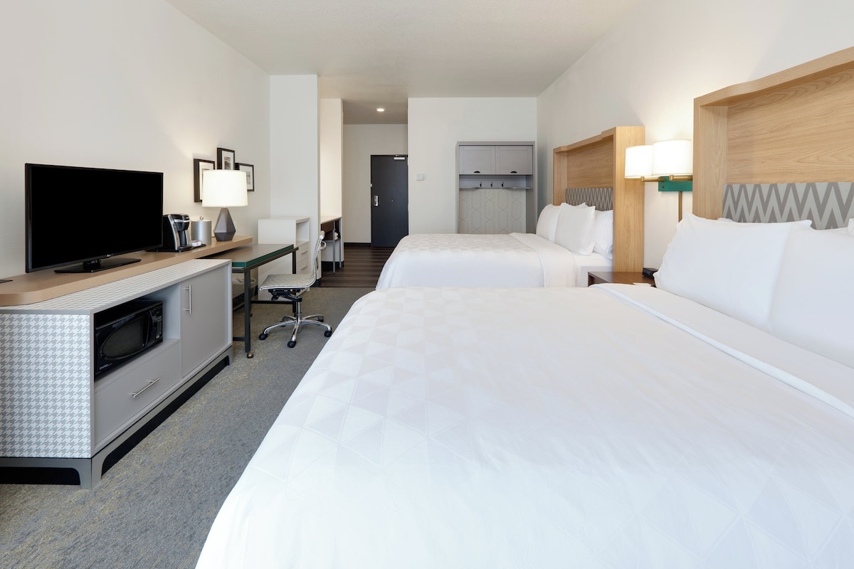Une chambre d’hôtel avec deux lits, un bureau avec un ordinateur, une télévision et un four à micro-ondes.