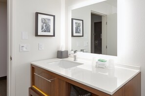 Une salle de bain moderne avec un lavabo blanc, un miroir, des œuvres d’art encadrées accrochées au mur et un distributeur de serviettes.