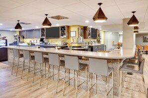 A modern bar area with a long counter, bar stools, and overhead pendant lighting. - Holiday Inn Twin Falls by IHG (Twin Falls)