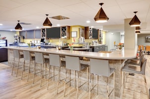 A modern bar area with a long counter, bar stools, and overhead pendant lighting.
