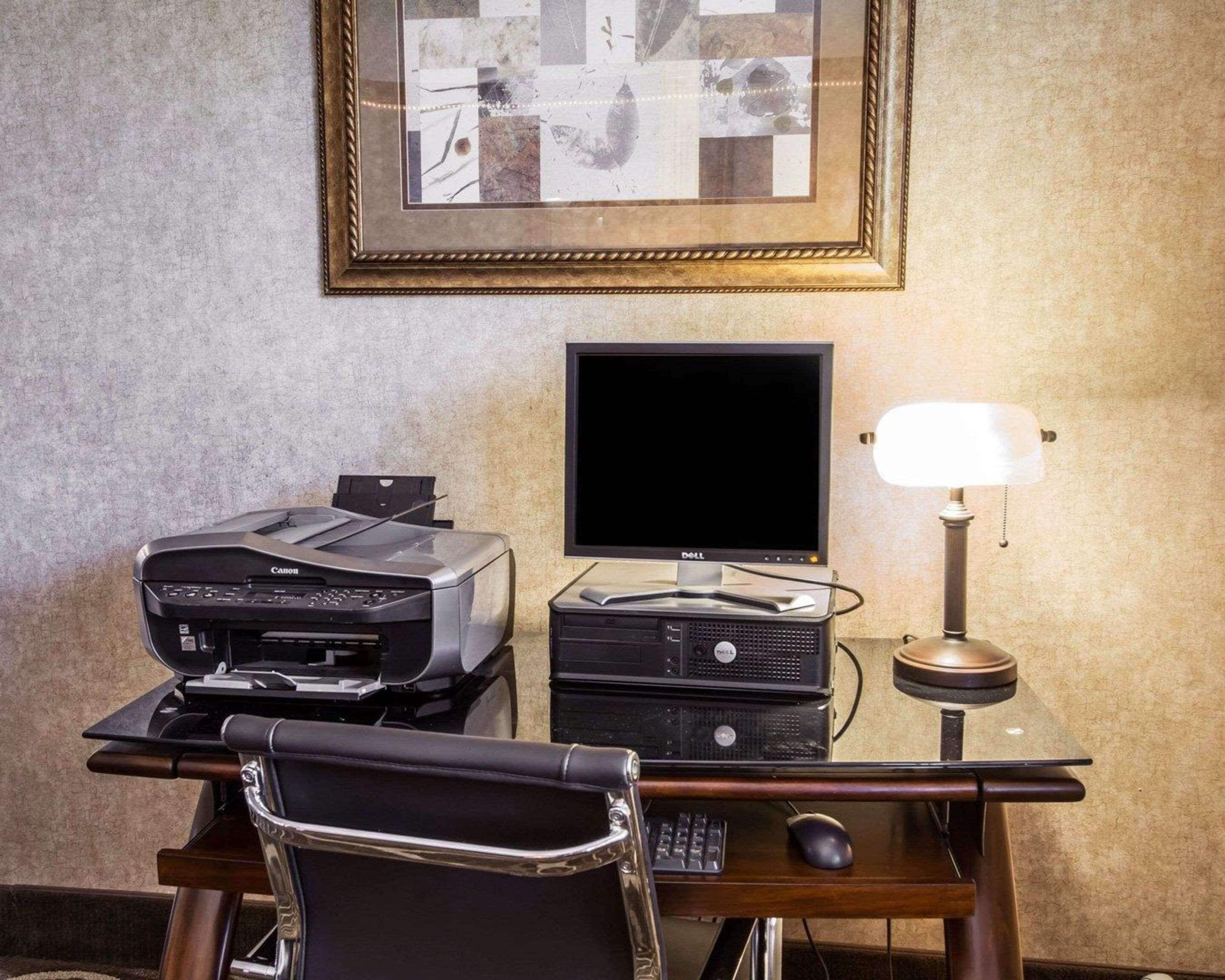 A hotel room desk with a Canon printer, a Dell monitor, a lamp, and a chair.