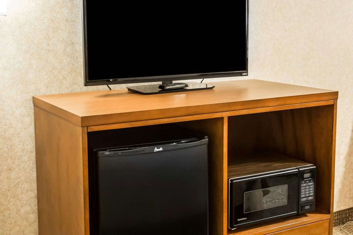 A wooden TV stand with a flat-screen TV, a mini fridge, and a microwave.